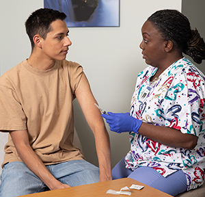 Healthcare provider giving teen boy injection in upper arm in exam room.