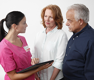 Health care provider with electronic tablet talking to woman and man.