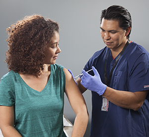 Health care provider giving injection in woman's arm.